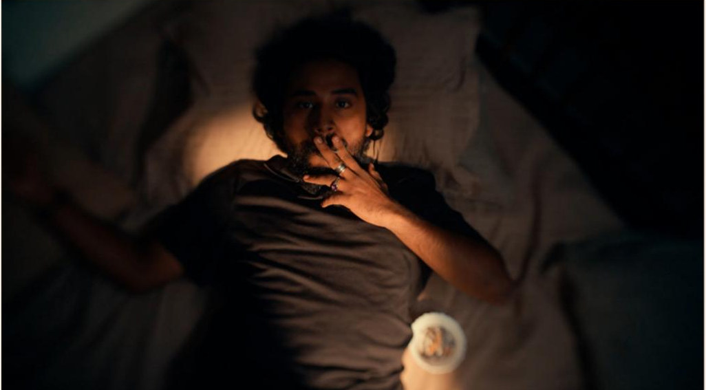 A sleepless man lying awake, lit by a phone screen