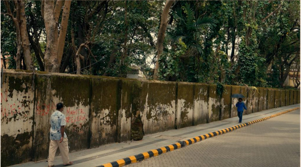 Two figures on opposite sides of a long roadside wall